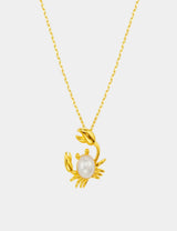 Gold crab-shaped pendant with a pearl on a gold chain against a white background